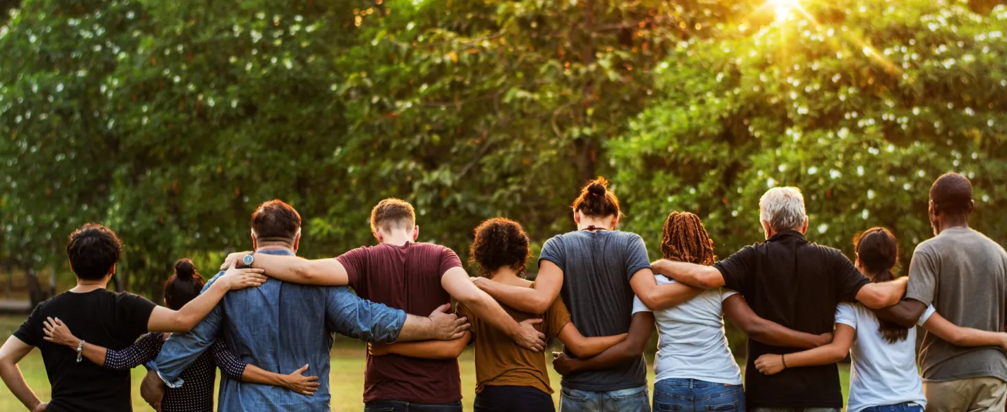 Diverse group of people standing together outdoors with arms around each other